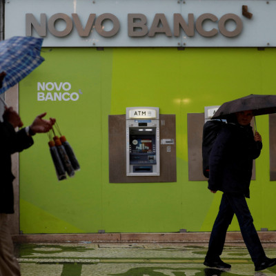 Um homem vende guarda-chuvas perto de caixas automáticos de uma sucursal do Novo Banco na baixa de Lisboa