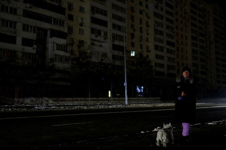 Mulher com um cachorro espera por um ônibus em uma rua sem eletricidade depois que a infraestrutura civil crítica foi atingida por ataques de mísseis russos em Kyiv