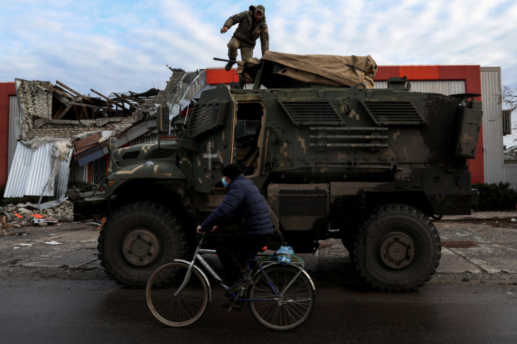 Um homem usando uma máscara facial protetora anda de bicicleta enquanto o ataque da Rússia à Ucrânia continua, passando por um soldado em um veículo militar americano MaxxPro na antiga cidade ocupada pela Rússia de Lyman, região de Donetsk na Ucrânia