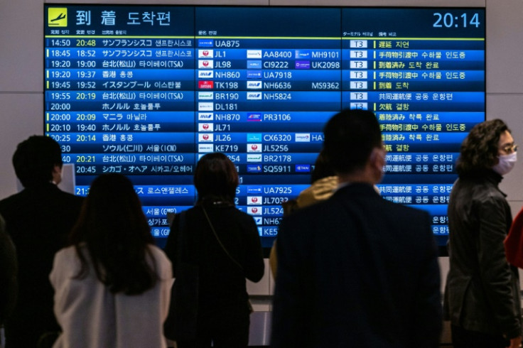 Pessoas esperam em frente a uma placa mostrando as chegadas de voos internacionais no aeroporto internacional de Haneda, em Tóquio
