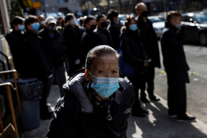 Uma mulher usando uma máscara facial protetora, em meio à pandemia da doença de coronavírus (COVID-19), caminha durante uma procissão fúnebre na seção Chinatown do bairro de Manhattan na cidade de Nova York, EUA, em 10 de fevereiro de 2022.
